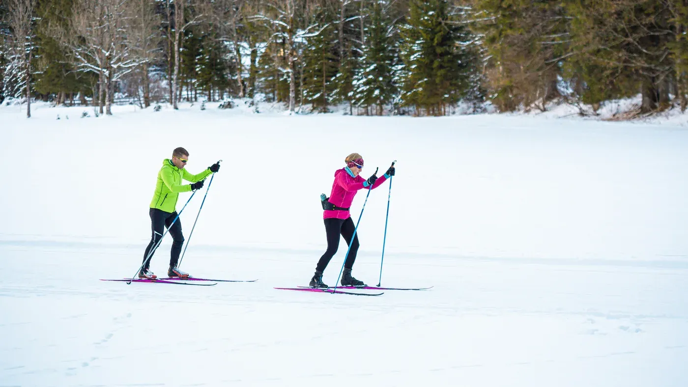 Två längdskidåkare åker klassiskt på ett snötäckt fält