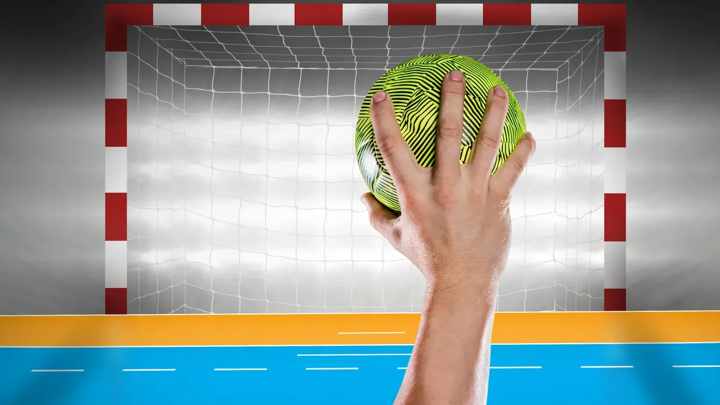 Hand som håller en handboll framför ett handbollsmål