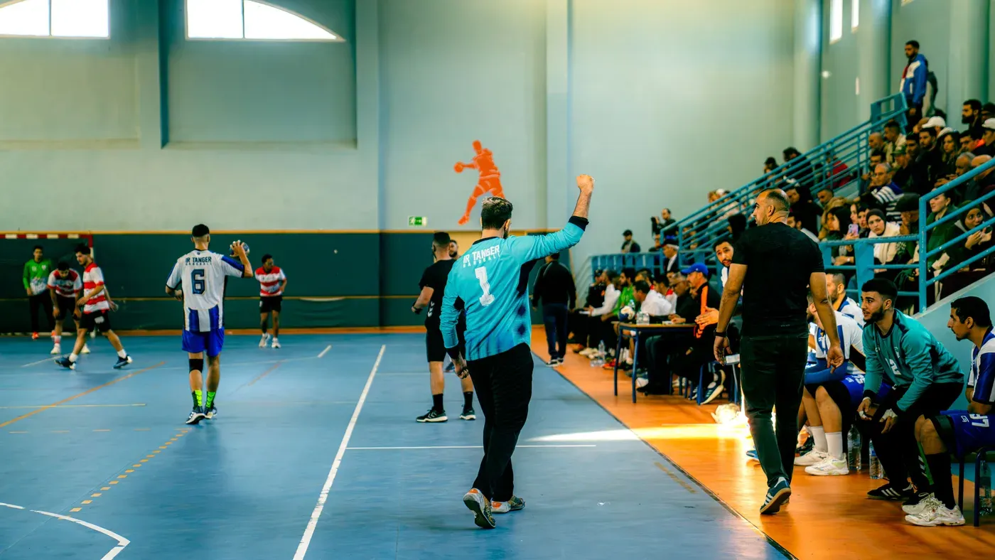 Målvakt i turkos tröja under en handbollsmatch i en idrottshall med publik