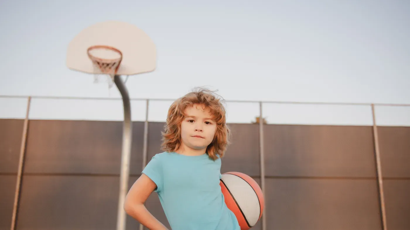 Barn håller en basketboll under en korg på en utomhusplan