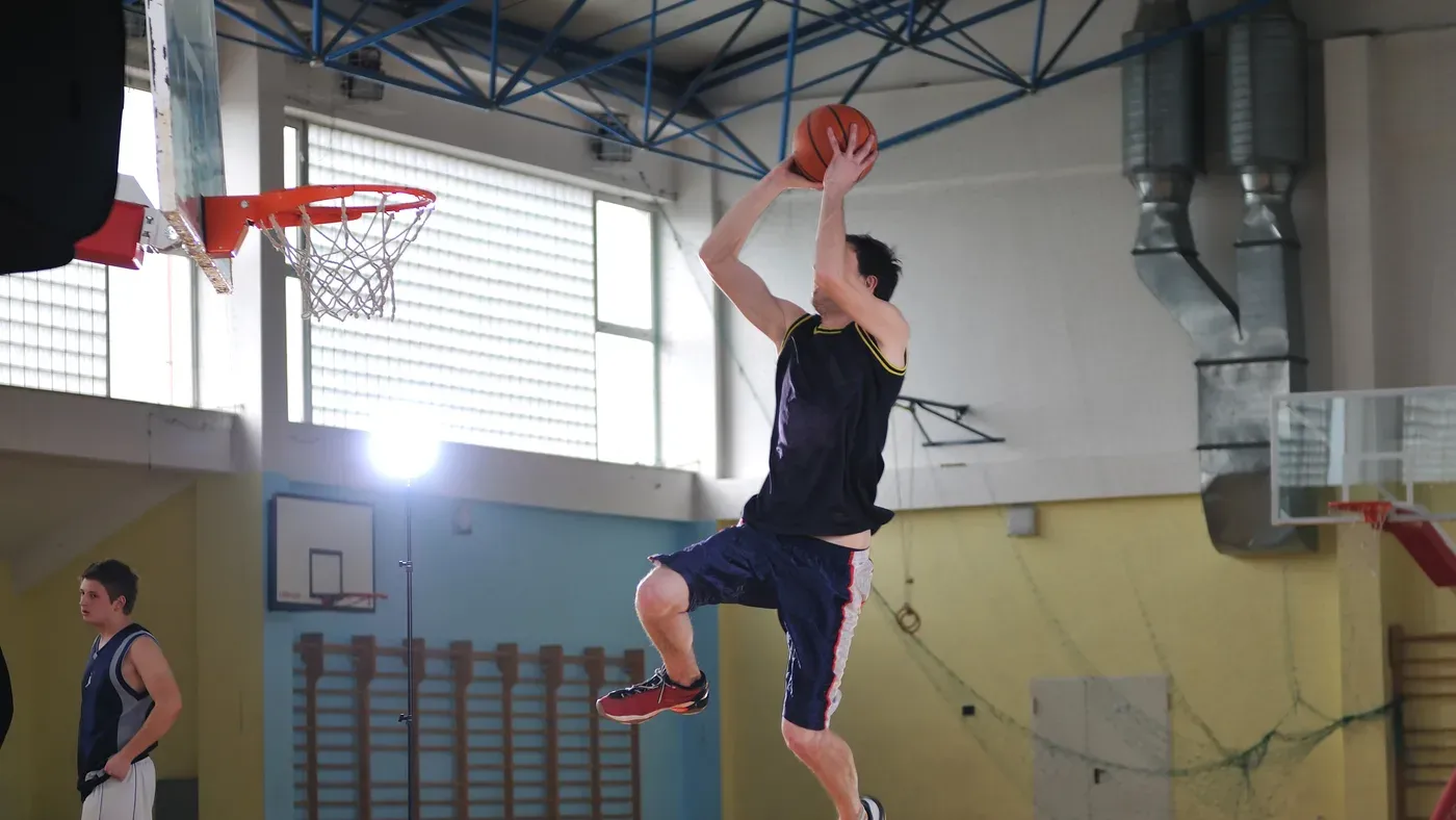 Basketspelare hoppar upp mot korgen med bollen ovanför huvudet i en idrottshall