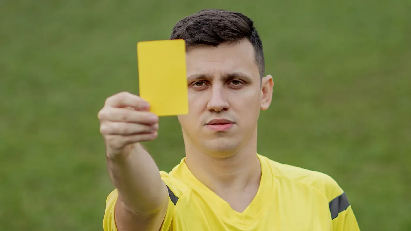 Domare i gul tröja visar ett gult kort under en fotbollsmatch