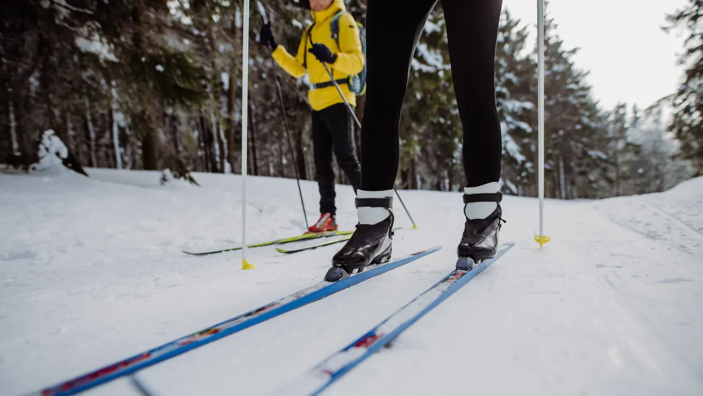 Två längdskidåkare på skidor i ett preparerat spår i skogen