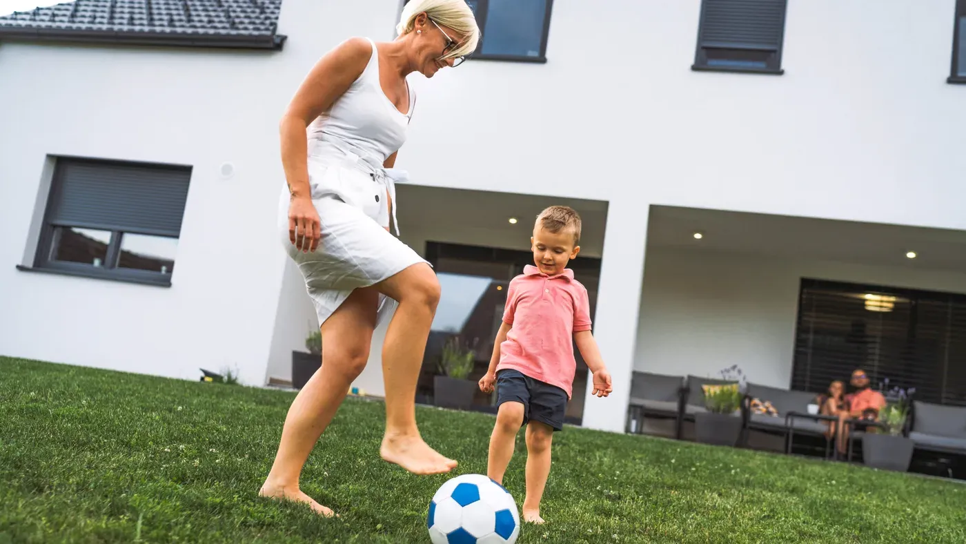 Förälder och barn spelar fotboll på gräsmattan i trädgården