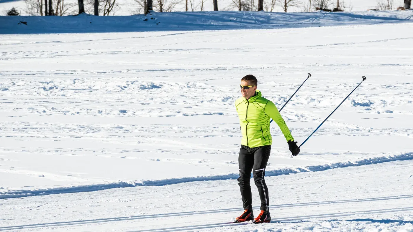 Längdskidåkare med stavar i ett preparerat skidspår i solsken